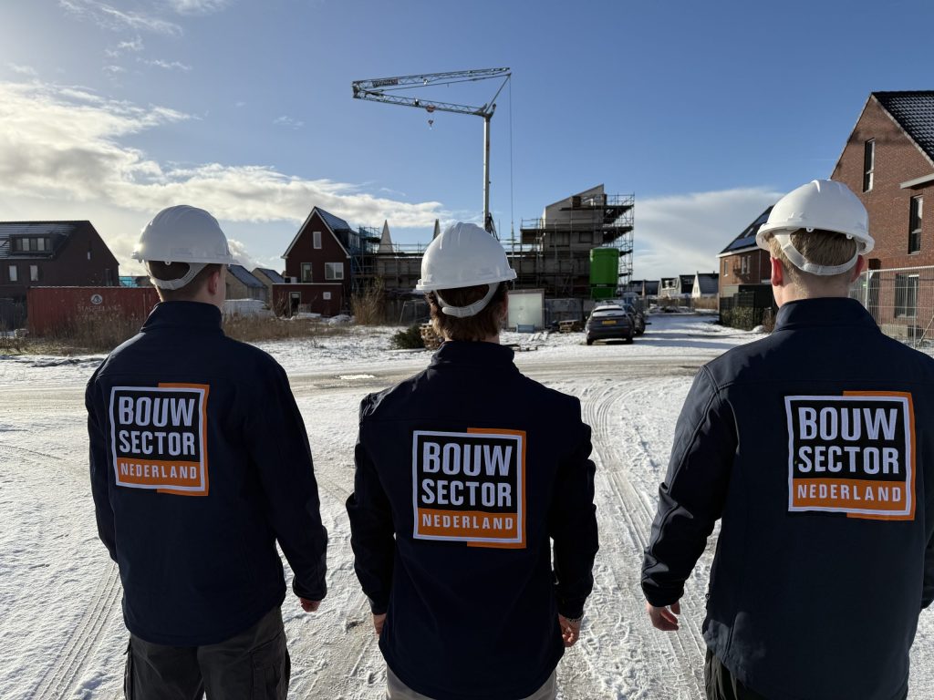 Drie mannen van achteren gezien met bedrijfsjas van Bouwsector Nederland voor een bouwkraan